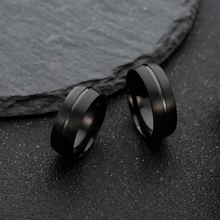 Two minimalist Matte Black Rings showcased against a contrasting dark, grainy backdrop.